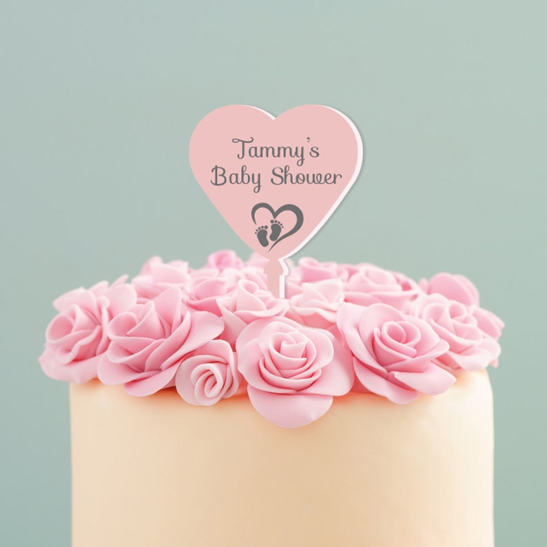 May include: Pink heart-shaped cake topper with the text "Tammy's Baby Shower" and a small footprint design.