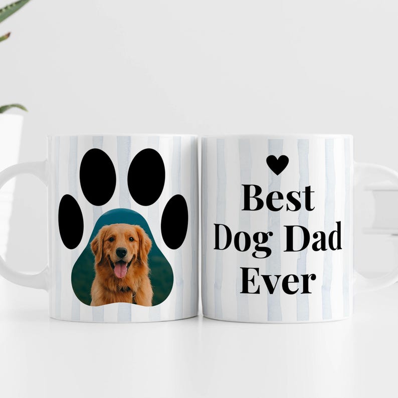 May include: White ceramic mug with a paw print design featuring a photo of a golden retriever. The other side of the mug has the text "Best Dog Dad Ever" with a heart symbol. The mug has a blue and white striped background.