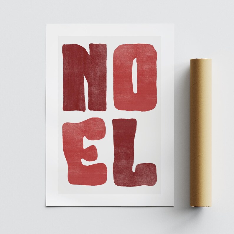 May include: A white print featuring the word "NOEL" in large, red, block letters. The letters have a textured appearance. A rolled-up brown poster is next to the print.