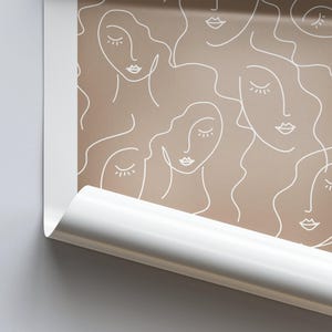 Op de afbeelding: Een naadloos patroon met een herhalend ontwerp van gestileerde gezichten met gesloten ogen en lippen. De gezichten zijn wit omlijnd en zijn geplaatst op een lichtbruine achtergrond.