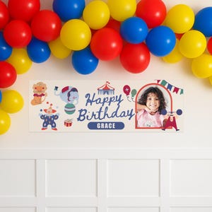 Puede incluir: Una pancarta de cumplea&ntilde;os rectangular con una foto de una ni&ntilde;a, ilustraciones de circo y el texto "Happy Birthday Grace". La pancarta es de color crema y est&aacute; decorada con globos rojos, azules y amarillos.