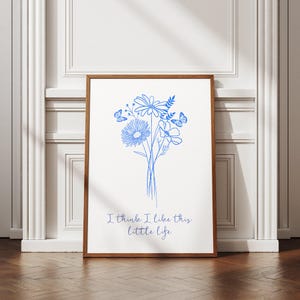 Puede incluir: Una impresi&oacute;n enmarcada en blanco con un dibujo de l&iacute;nea azul de un ramo de flores y mariposas. El texto "I think I like this little life" est&aacute; escrito debajo de las flores.