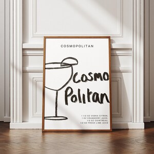 May include: A black and white illustration of a cocktail glass with a lime wedge on top. The text "COSMOPOLITAN" is at the top of the image. The text "COSMO Politan" is written in a stylized font below the glass. The recipe for a Cosmopolitan cocktail is listed below the text: 1 1/2 oz vodka citron, 1 oz cranberry juice, 1/2 oz Cointreau, 1/2 oz fresh lime juice.