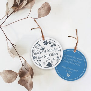 May include: Two round, white and blue gift tags with twine. The white tag has a floral design and the text "You're a Mother Like No Other". The blue tag has the text "We Hope You Have An Amazing Day Lots of Love From Amy Jamee And Bailey" with a small flower.