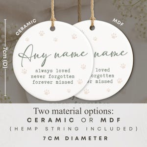 May include: Two round, white ceramic and MDF ornaments with hemp string. Each ornament has a paw print design and the words "Any name" in script. The text "always loved, never forgotten, forever missed" is also printed. The diameter is 7cm.