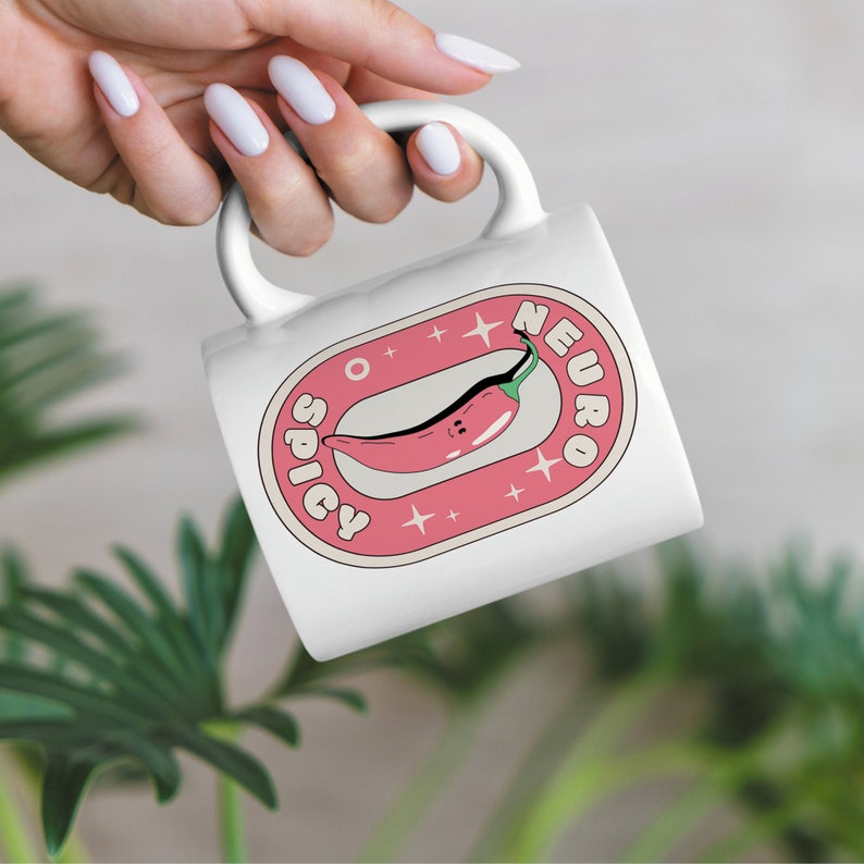 Puede incluir: Taza de cer&aacute;mica blanca con un gr&aacute;fico rosa y blanco de un chile rojo con una cara sonriente. El gr&aacute;fico dice "Spicy Neuro" con estrellas alrededor del chile.