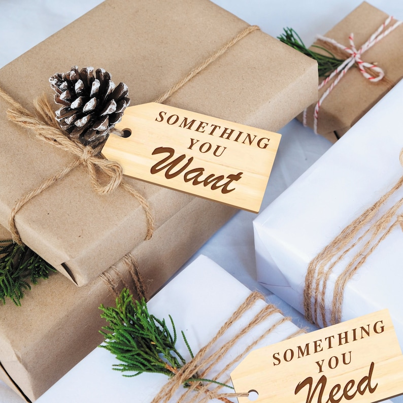 K&ouml;nnte beinhalten: Zwei verpackte Geschenke mit Holz-Geschenk-Etiketten. Das Etikett auf der braunen Geschenkbox lautet "Something You Want". Das Etikett auf der wei&szlig;en Geschenkbox lautet "Something You Need".