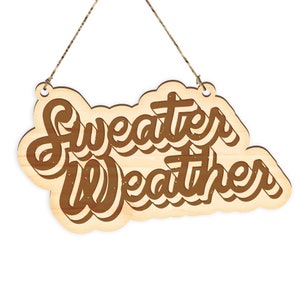 May include: Wooden sign with the words "Sweater Weather" in a brown, layered font. The sign is shaped like a cloud and hangs from a natural twine string. The wood has a light, natural finish.