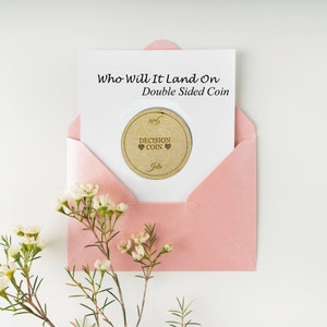 May include: A pink envelope holds a white card with the text "Who Will It Land On Double Sided Coin." A circular decision coin with the words "Decision Coin" and two hearts is visible. The coin is personalized with the name "Julie."