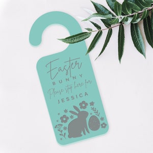 May include: A teal blue door hanger with the text "Easter Bunny Please stop here for Jessica" and a gray silhouette of a bunny rabbit with flowers and an egg.