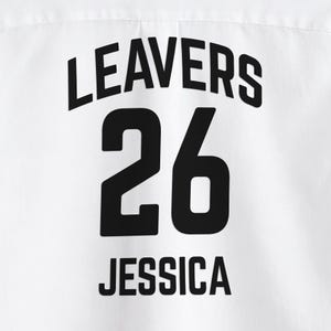May include: White fabric with the black text "LEAVERS 26 JESSICA". The number 26 is centered below the word "LEAVERS". The name "JESSICA" is centered below the number 26.