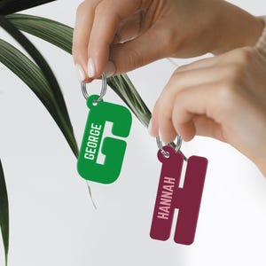 May include: Two personalized keychains with the names "GEORGE" and "HANNAH" in white lettering. The keychain with "GEORGE" is green and the keychain with "HANNAH" is burgundy.