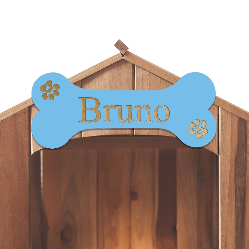 May include: A wooden dog house with a blue bone-shaped sign above the entrance. The sign has the name "Bruno" written on it in gold letters and paw prints on either side.