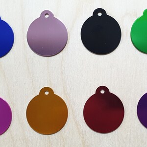 May include: Eight round metal tags in different colors: blue, purple, silver, black, green, gold, red, and purple. Each tag has a small hole at the top for attaching a ring or chain.