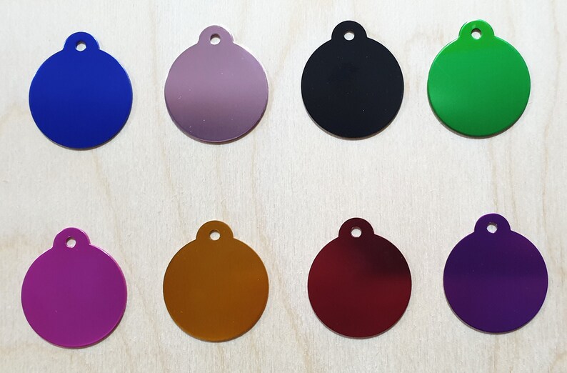 May include: Eight round metal tags in different colors: blue, purple, silver, black, green, gold, red, and purple. Each tag has a small hole at the top for attaching a ring or chain.