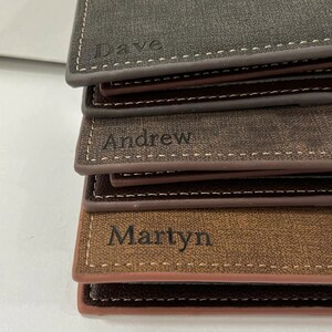 May include: Three brown leather wallets stacked on top of each other. The top wallet has the name "Dave" engraved on it. The middle wallet has the name "Andrew" engraved on it. The bottom wallet has the name "Martyn" engraved on it.