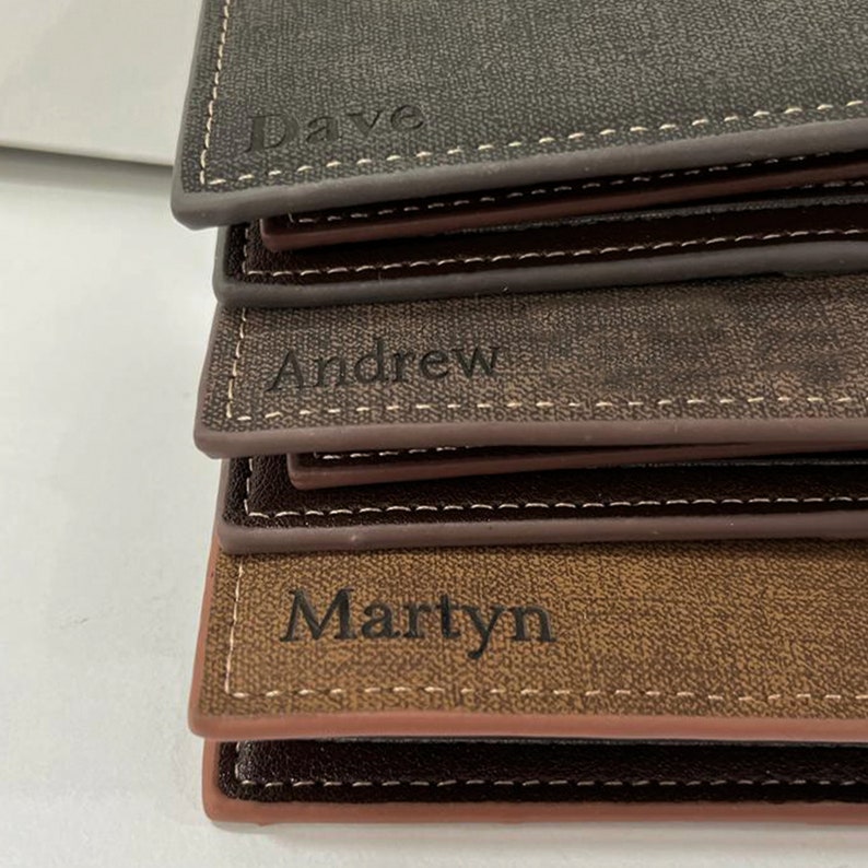 May include: Three brown leather wallets stacked on top of each other. The top wallet has the name "Dave" engraved on it. The middle wallet has the name "Andrew" engraved on it. The bottom wallet has the name "Martyn" engraved on it.