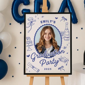 May include: A graduation party sign featuring a photograph of a young woman, adorned with blue illustrations of party elements. The sign displays "Emily's Graduation Party 2025" in a decorative font, framed in black and presented on a wooden easel.