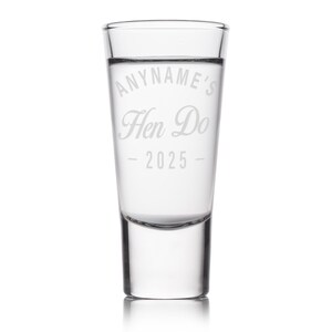 May include: A clear shot glass with the text "ANYNAME'S Hen Do - 2025" etched on the front. The glass is cylindrical with a thick base and is filled with a clear liquid.