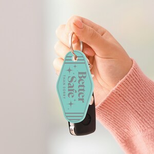 May include: A turquoise blue key chain with a motel key tag that says "Better Safe Than Sorry" in gray text with a retro font. The key tag has a white border and two white stars on each side of the text.