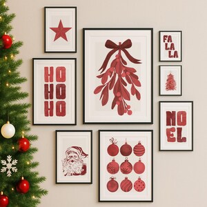 May include: A collection of framed Christmas-themed art prints. The prints feature festive imagery such as a red star, mistletoe, Christmas ornaments, and the words "HO HO HO", "FA LA LA", and "NOEL". The art is in red and white.