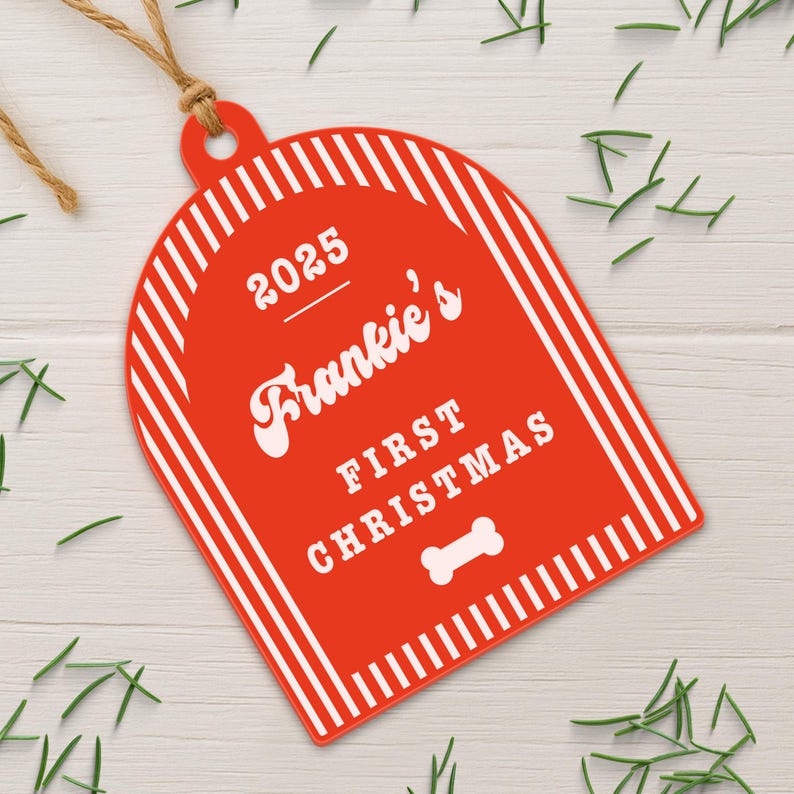 May include: A red Christmas ornament with white vertical stripes and the text "2025 Frankie's FIRST CHRISTMAS" in white. A white bone graphic is at the bottom. The ornament is hanging by a brown string.