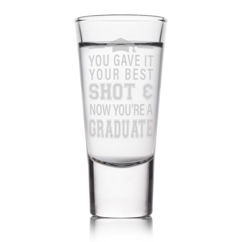 May include: Clear shot glass with etched text: "YOU GAVE IT YOUR BEST SHOT & NOW YOU'RE A GRADUATE." The glass features a graduation cap graphic above the text. A celebratory gift for a recent graduate.