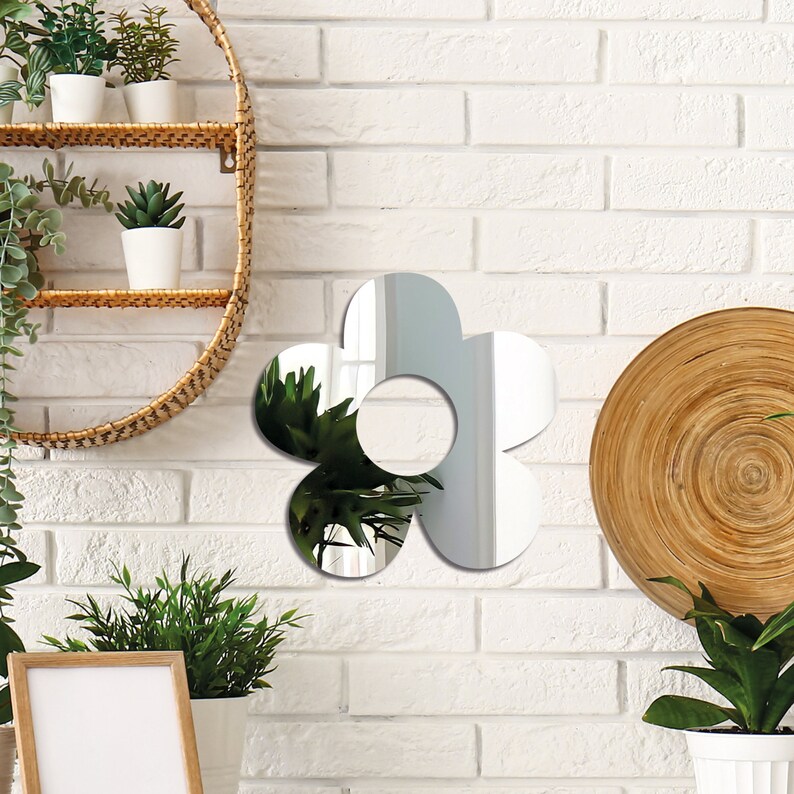 May include: A silver flower-shaped mirror with a rounded center hole. The mirror is hanging on a white brick wall.