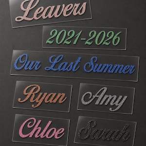 May include: A collection of clear rectangular labels with glitter text. The labels display phrases like "Leavers" and "Our Last Summer," along with names such as "Ryan" and "Amy." The text colors include pink, green, blue, orange, silver, and black.