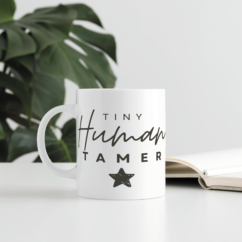 May include: White ceramic mug with black text that reads "Tiny Human Tamer" and a black star graphic.