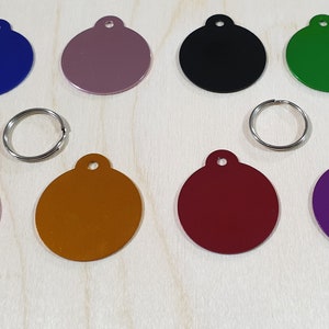 May include: Ten round metal tags in various colors, including purple, pink, red, orange, gold, black, green, blue, and two shades of gray. The tags have a hole at the top for attaching to a key ring or collar.