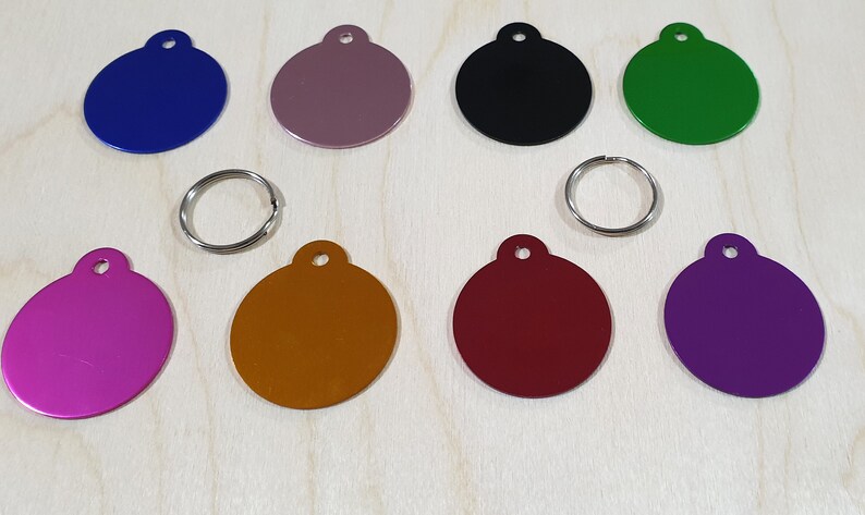 May include: Ten round metal tags in various colors, including purple, pink, red, orange, gold, black, green, blue, and two shades of gray. The tags have a hole at the top for attaching to a key ring or collar.