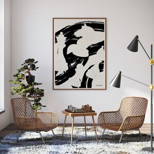May include: A black and white abstract art print with the word "Checkmate" in the bottom right corner. The print is framed and hanging on a white wall in a living room setting. Two wicker chairs and a small table with a chessboard are in the foreground.