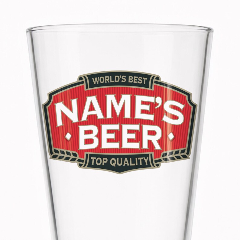 May include: A clear beer glass with a red and white label. The label reads "WORLD'S BEST NAME'S BEER TOP QUALITY" in white text with black and gold accents. The glass has a slightly tapered shape.
