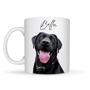 May include: White ceramic mug featuring a black Labrador Retriever with its tongue out. The dog is wearing a black collar. The name "Bella" is written in cursive above the dog's head.