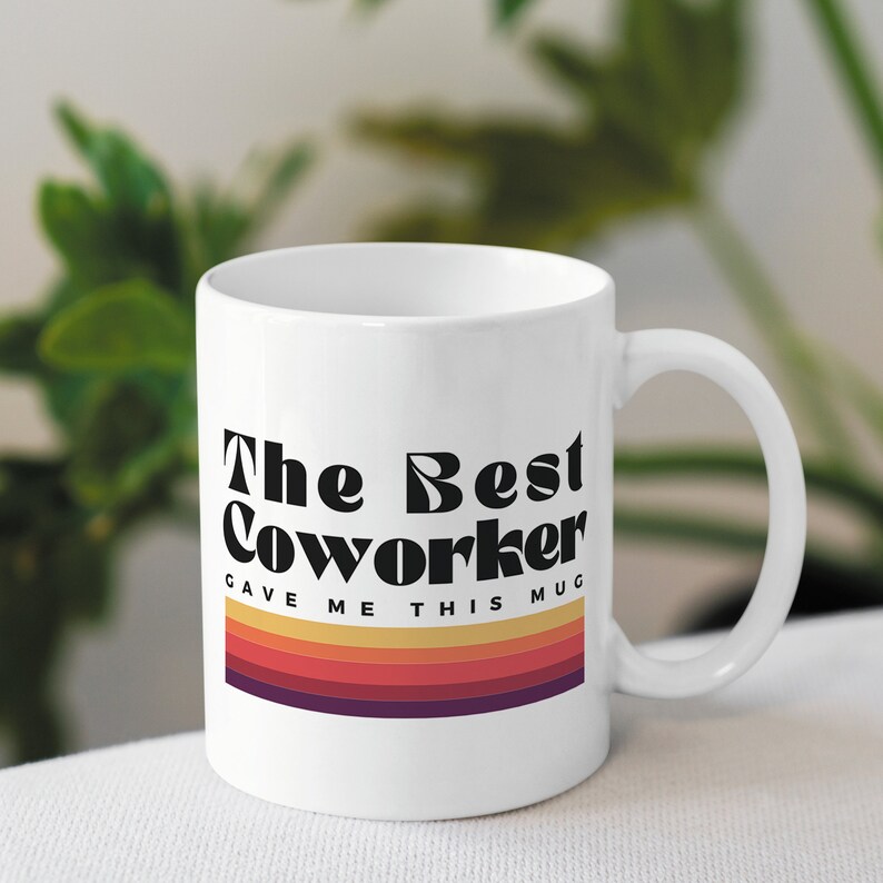 May include: White ceramic mug with black text that reads "The Best Coworker Gave Me This Mug" with a retro-style rainbow stripe design.
