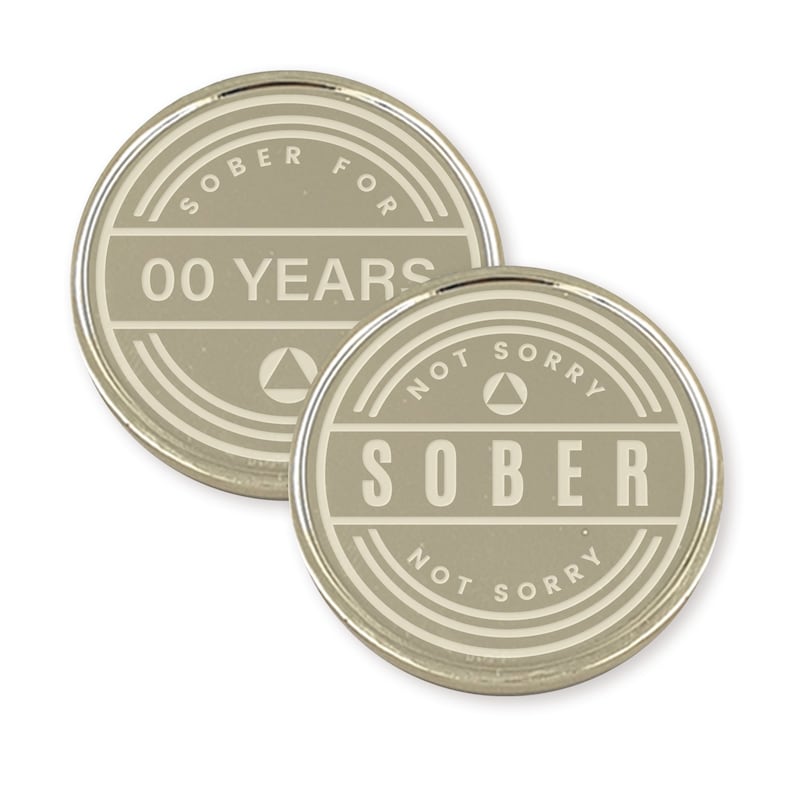 May include: Two silver-colored metal coins with a white design. The first coin says "Sober for 00 Years" with a triangle symbol. The second coin says "Not Sorry Sober Not Sorry" with a triangle symbol.