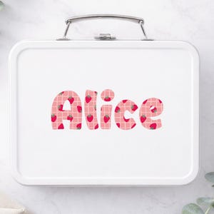 May include: White metal lunchbox with a silver handle. The name "Alice" is printed in large, bubble letters across the front. The letters are pink with a strawberry pattern and a white grid design.