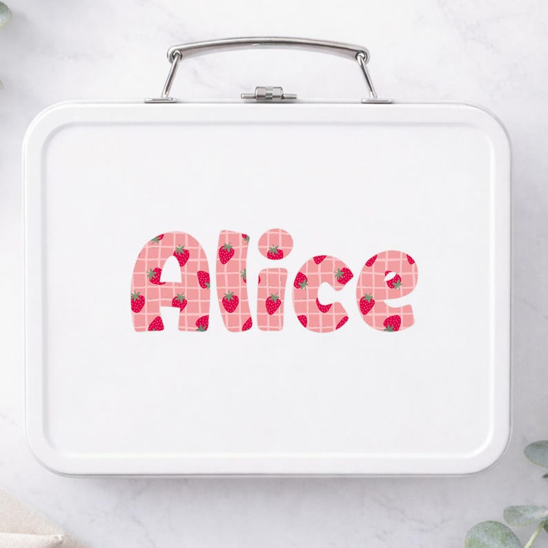 May include: White metal lunchbox with a silver handle. The name "Alice" is printed in large, bubble letters across the front. The letters are pink with a strawberry pattern and a white grid design.