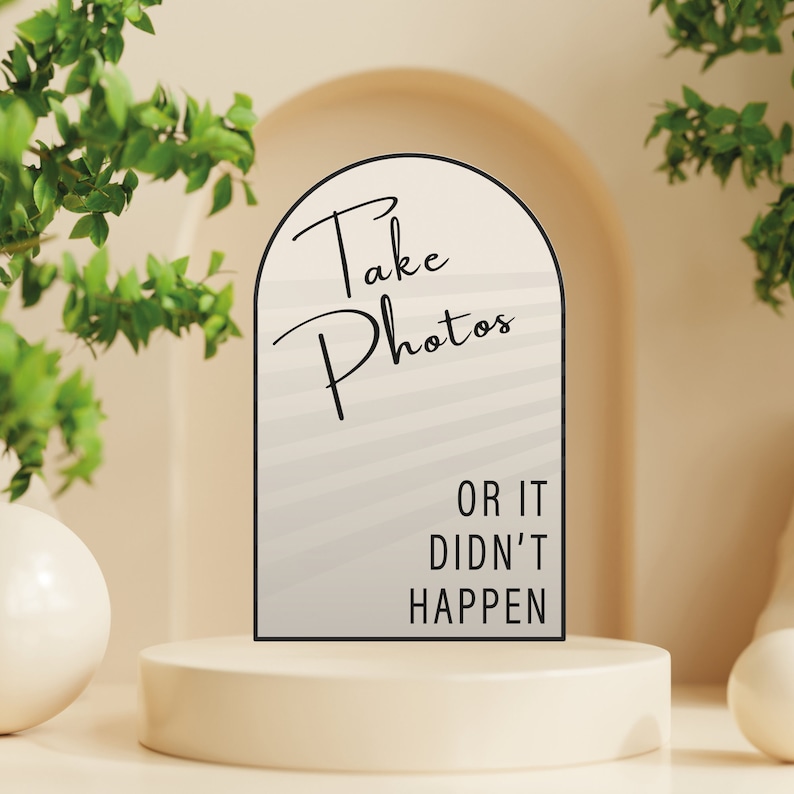 以下が含まれることがあります： 「Take Photos or it didn't happen」と黒文字で書かれた白い看板。看板はアーチ型で、グレーと白のストライプ模様の背景があります。