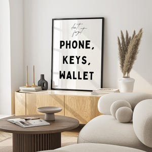 May include: A black and white framed print with the text "Don't forget PHONE, KEYS, WALLET" hanging on a white wall above a wooden cabinet. The print is in a modern minimalist style.