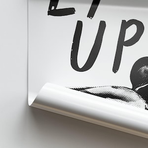 Op de afbeelding: Zwart-witte poster met de tekst "Eat Up" in vetgedrukte, handgeschreven letters. De poster toont een zwart-witte afbeelding van een persoon met zijn hoofd naar achteren gekanteld, alsof hij eet.