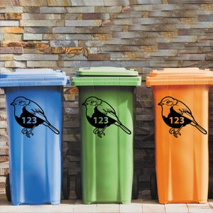 May include: Three colorful trash cans: blue, green, and orange. Each can features a black bird silhouette with the number "123" on its belly. The cans are set against a textured brick wall background.