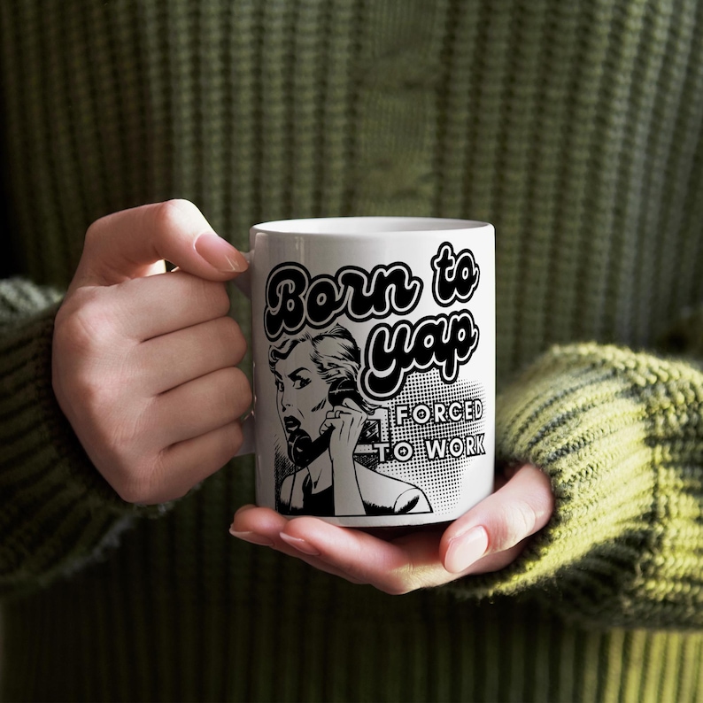 May include: White ceramic mug with a black and white illustration of a woman on the phone. The text on the mug reads "Born to yap forced to work".
