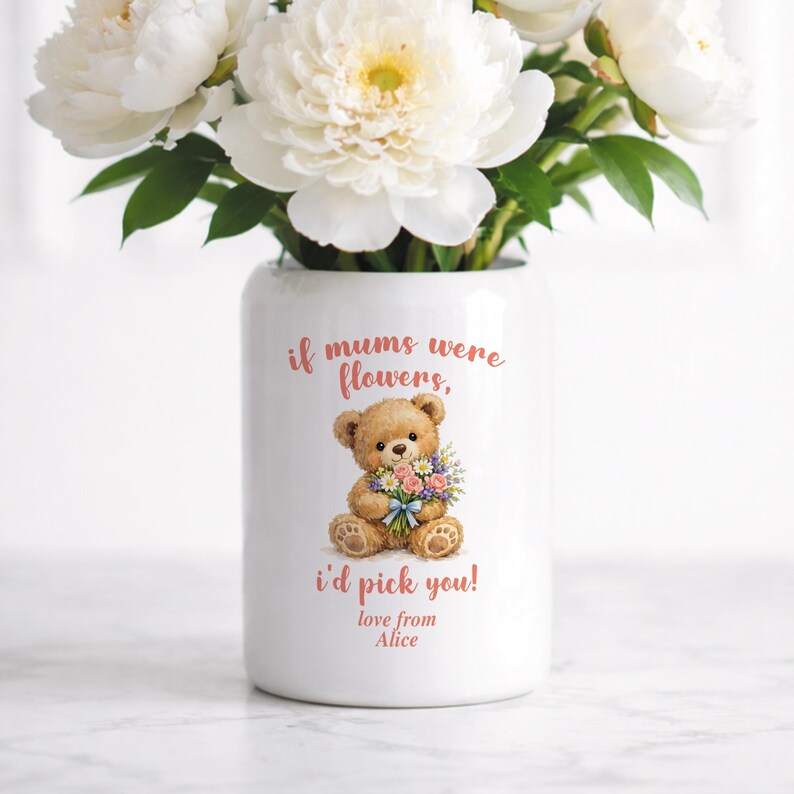May include: A white ceramic vase with a floral arrangement of white peonies. The vase features a teddy bear illustration holding flowers, with the text "if mums were flowers, I'd pick you! love from Alice."