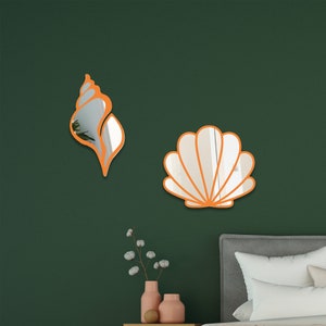 May include: Two decorative wall mirrors shaped like seashells. The larger mirror is a white seashell with an orange outline. The smaller mirror is an orange seashell with a reflective surface.