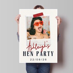 May include: A poster with a photo of a woman wearing heart-shaped sunglasses, sticking out her tongue, and holding a drink. The poster reads "Ashleigh's HEN PARTY" with the date "22/08/26" below. A red tape is at the top.