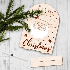 May include: A wooden sign with a cutout of Santa's face and the text "Sleep's Until Christmas". The sign is decorated with snowflakes and a holly sprig.