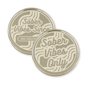 May include: Two silver-colored metal tokens with a white design. One token says "Sober Vibes Since" with a blank space for a date. The other token says "Sober Vibes Only".