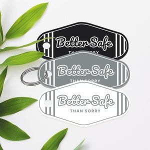 May include: Three keychains with a black, grey, and white background. Each keychain has a white stripe pattern and the text "Better Safe Than Sorry" in a white, grey, and black font.
